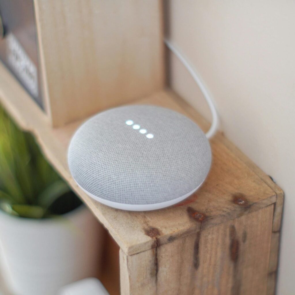 A Google Home Mini smart speaker on a wooden shelf, blending technology with home decor.